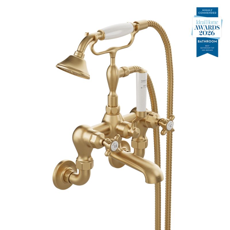 Booth & Co. Axbridge wall mounted bath shower mixer tap with shower kit and cross handles, finished in brushed brass with crackled off-white ceramic accents.