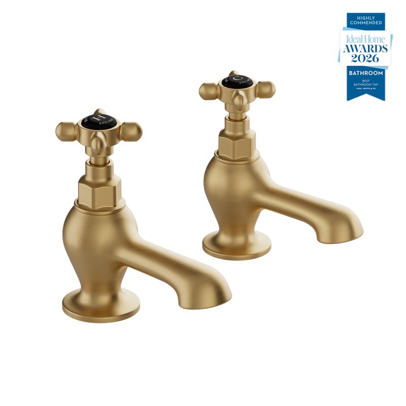 Booth & Co. Axbridge bath pillar taps with cross handles, finished in brushed brass with black ceramic accents.
